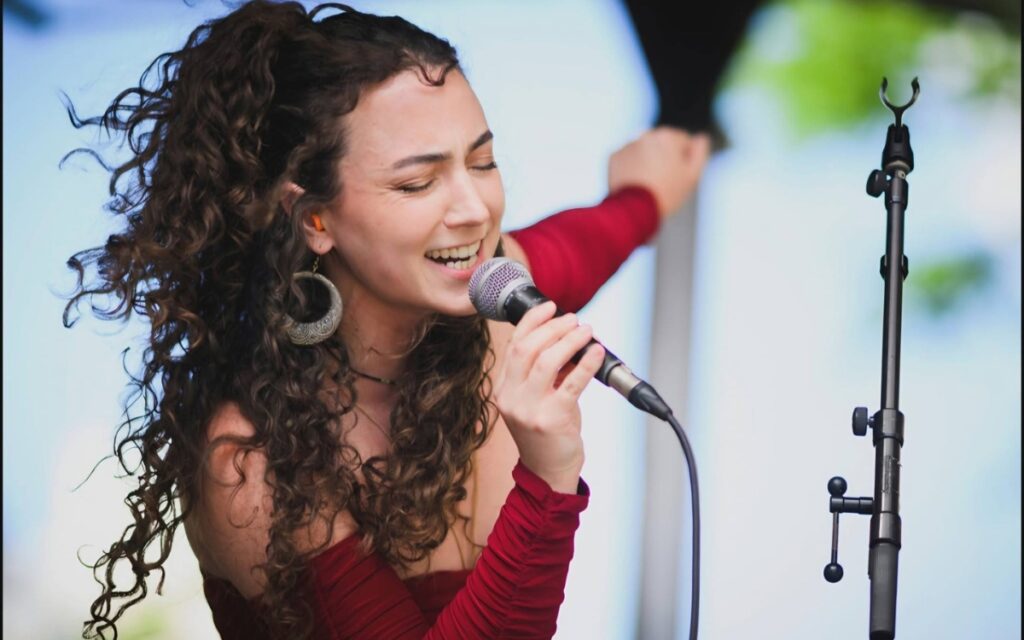 A woman with long brown curly hair holds a microphone as she dances and sings during the Ladybug Festival.
