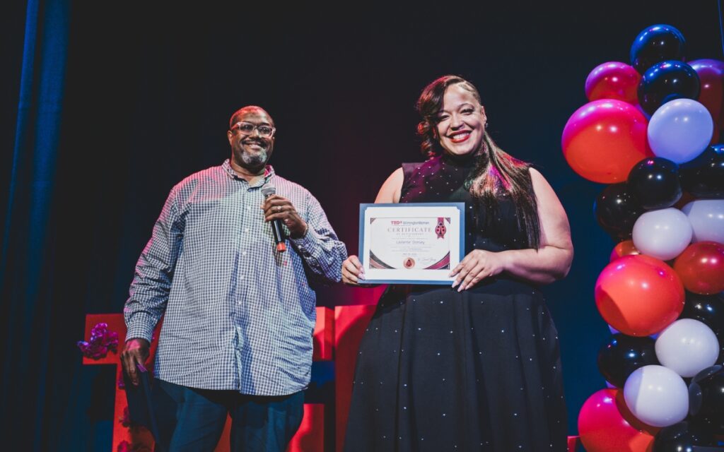 Dr. Dan Young smiles as he stands behind LaVanté Dorsey, who is beaming with pride as she holds up her TEDxWilmington Certificate of Achievement.